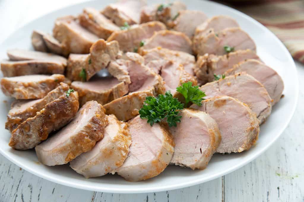 A white plate with slices of keto pork tenderloin arranged in a spiral.