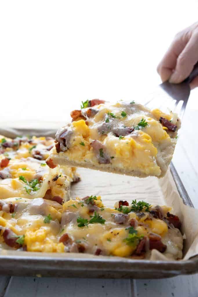 A spatula living a slice of keto breakfast pizza up off the pan.