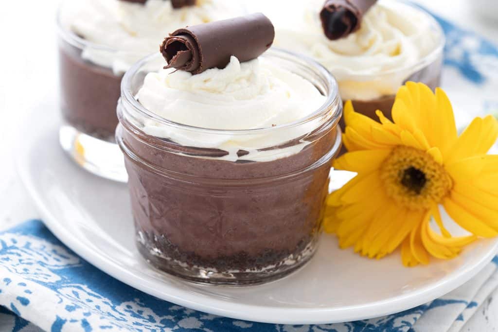 3 mini chocolate cream pies on a white plate with a yellow flower beside them.