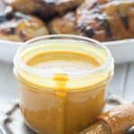 A jar full of Carolina Mustard Barbecue Sauce in front of a plate of grilled chicken.