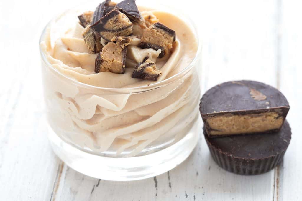 A cup filled with sugar free peanut butter mousse with chopped peanut butter cups on top.