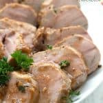 Titled image of slices of pork tenderloin on a white plate, drizzled with garlicky sauce.