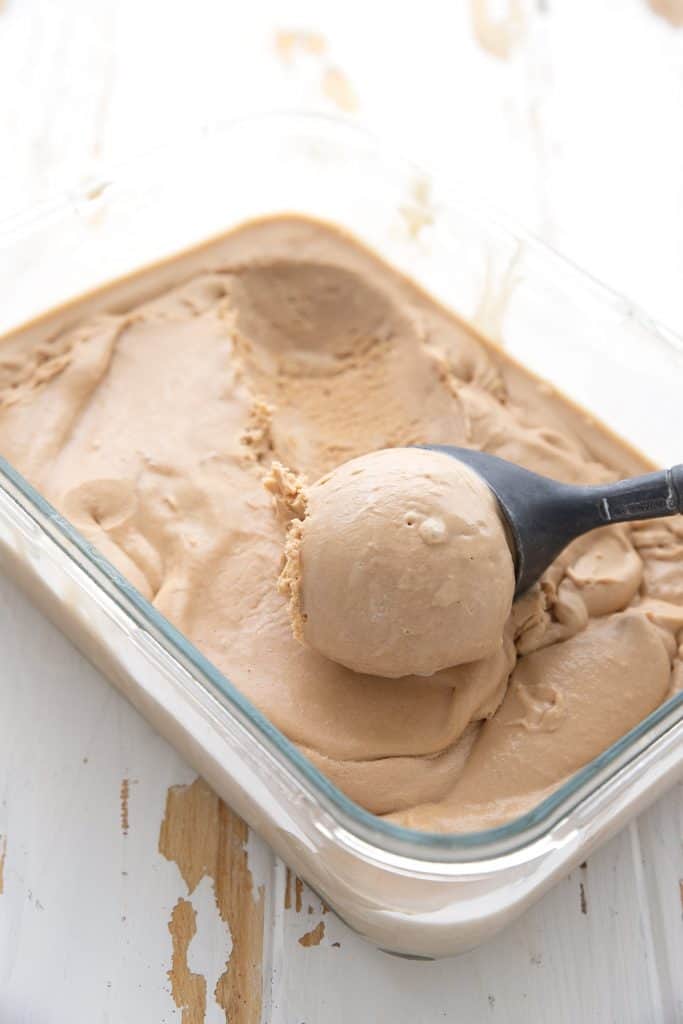 A container of keto salted caramel ice cream with an ice cream scoop lifting some out.