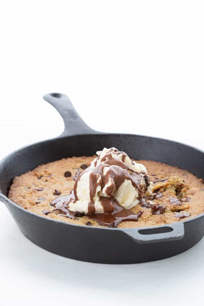 Keto skillet cookie in a cast iron skillet on a white background, topped with keto ice cream and chocolate sauce.