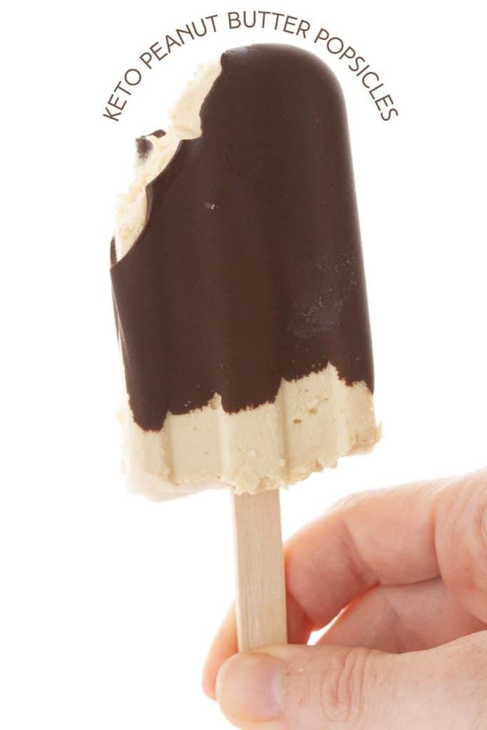 Titled image of a hand holding up a peanut butter popsicle with a bite taken out of it.