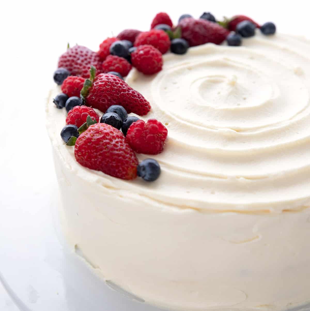 Keto Chantilly Cake on a white cake plate with berries on top.