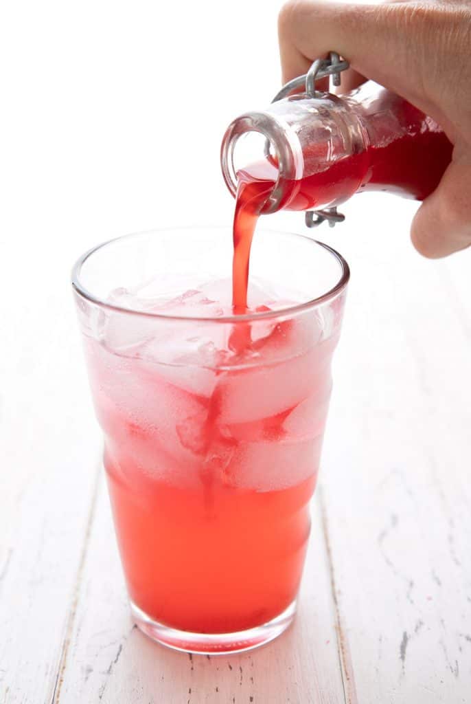 Sugar free raspberry syrup being poured into a glass of Italian soda
