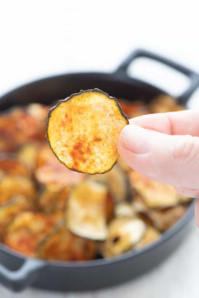 A hand holding up a zucchini chip to show how thin and crisp it is.