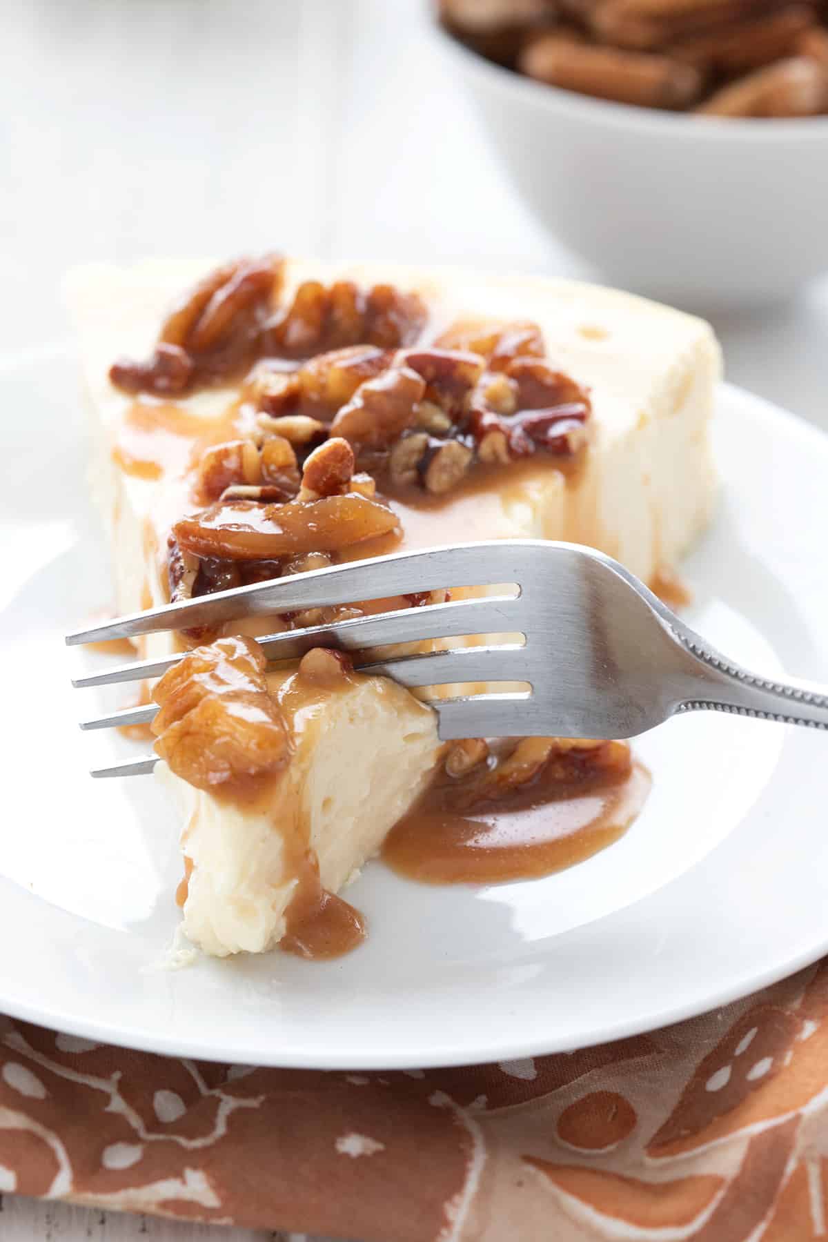 A fork digging into a slice of keto cheesecake with sugar free praline sauce on top.