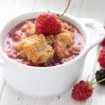 Close up shot of keto cobbler in a white ramekin with berries around it.