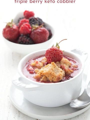 Titled image of triple berry keto cobbler in a white ramekin, with a bowl of berries in the background.