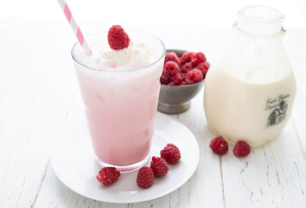 Keto Italian Cream Soda in a glass with a bowl of raspberries and a jar of cream.