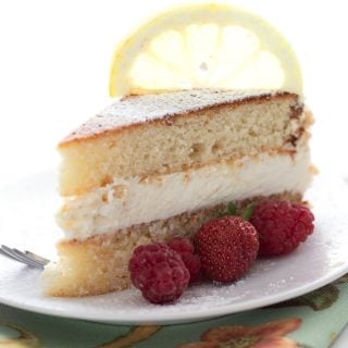 A slice of keto lemon cake on a white plate with berries on the side and a lemon slice on top.