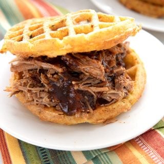 A keto pulled pork sandwich on low carb waffles, on a white plate over a colourful striped napkin.