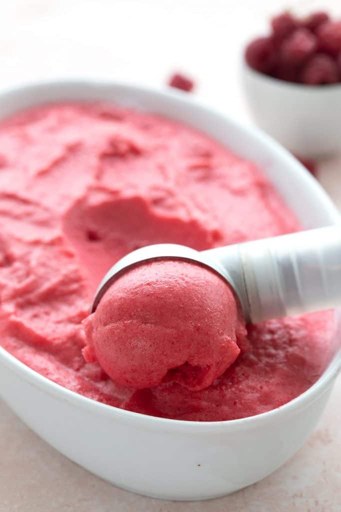 Close up shot of an ice cream scoop scooping out raspberry keto sorbet.