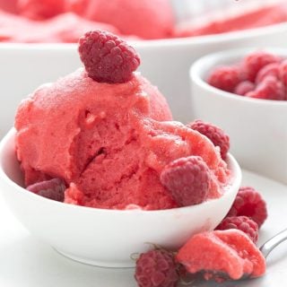 Titled image of a bowl of sugar free raspberry sorbet in a white bowl with a spoonful taken out.