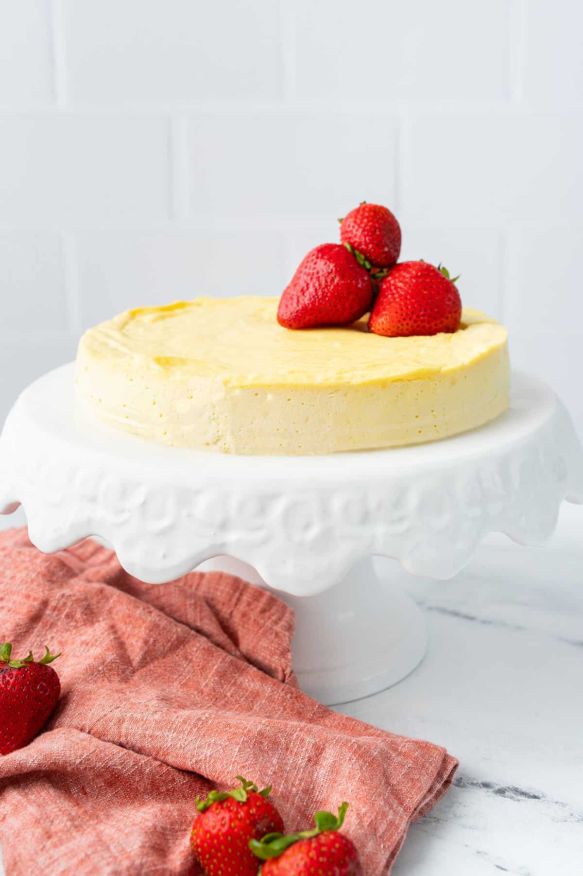 Crustless Keto Cheesecake on a white cake stand with strawberries on top. 
