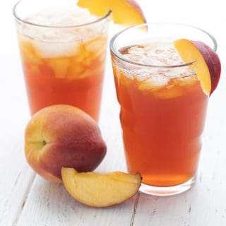 Two glasses of sweet peach tea on a white table with sliced peaches.