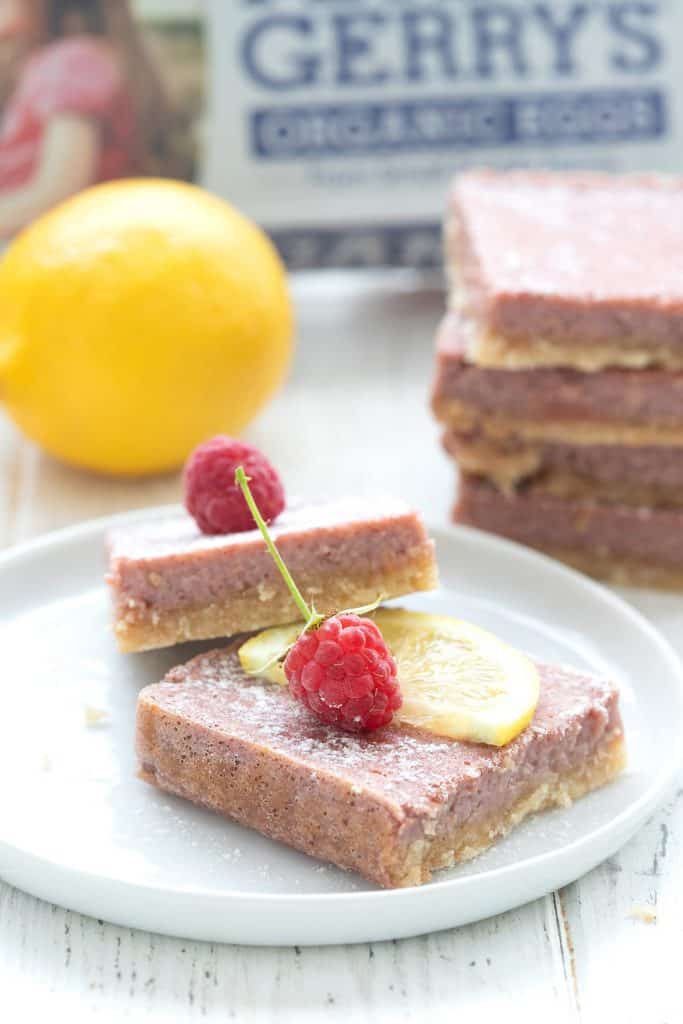 Raspberry lemonade bars on a white plate with raspberries and lemon slices on the top.