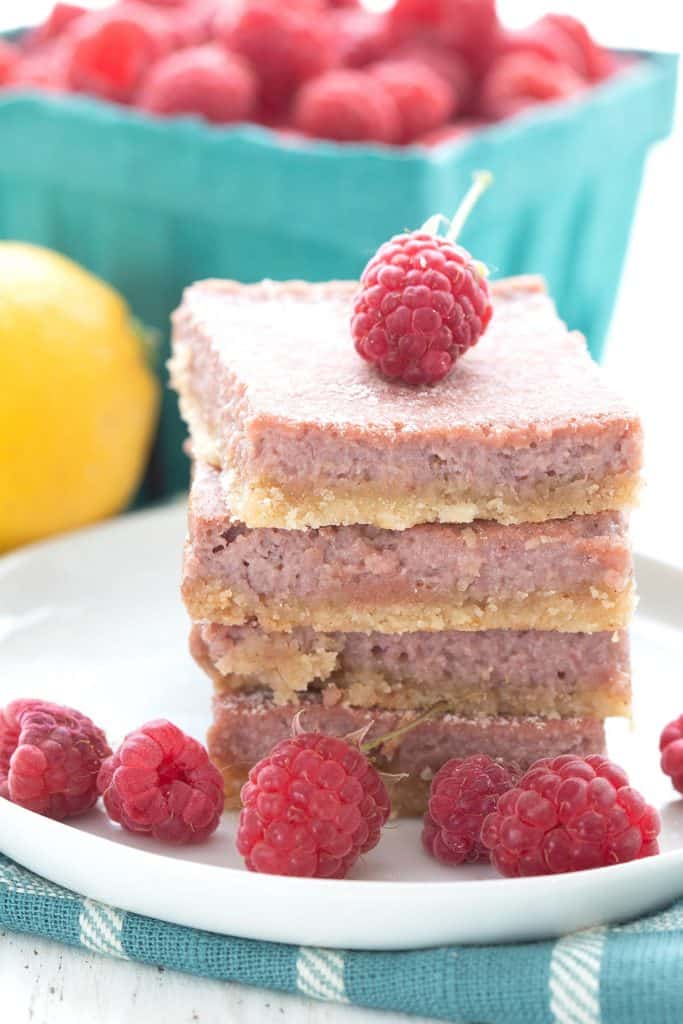 A stack of keto raspberry bars on a white plate topped with a fresh raspberry.
