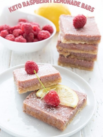 Titled image of keto raspberry lemonade bars on a white plate with a bowl of raspberries and a lemon in the background.