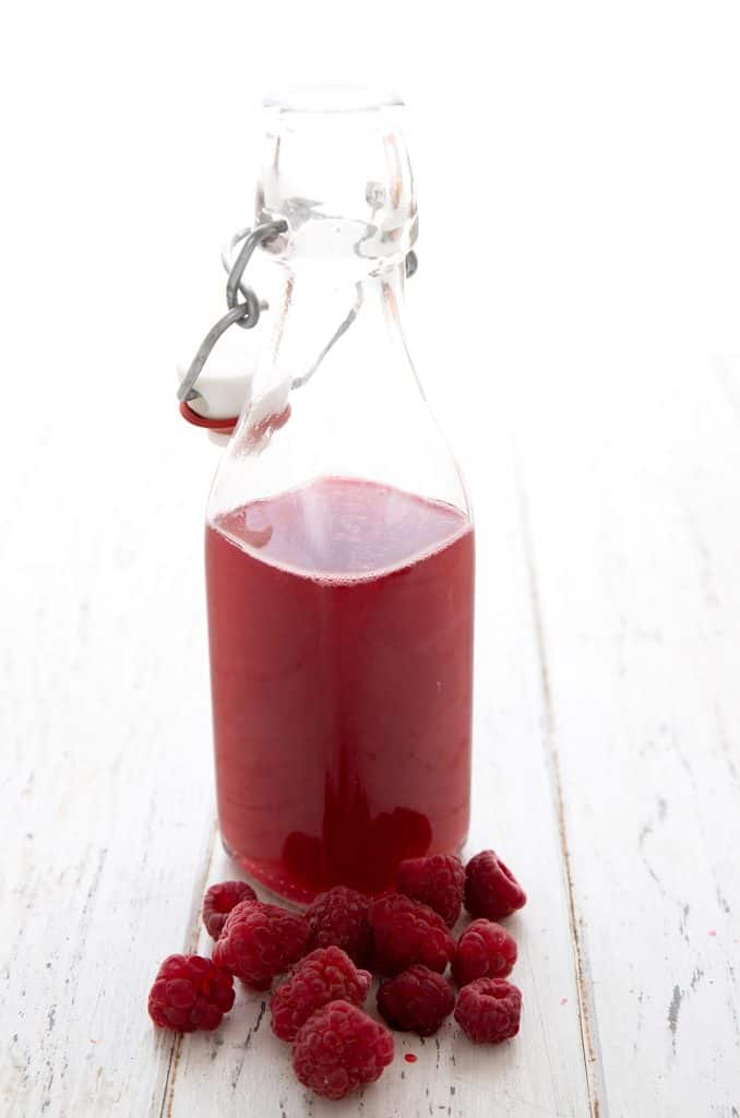 Sugar free raspberry simple syrup in a glass bottle with raspberries around the bottom.