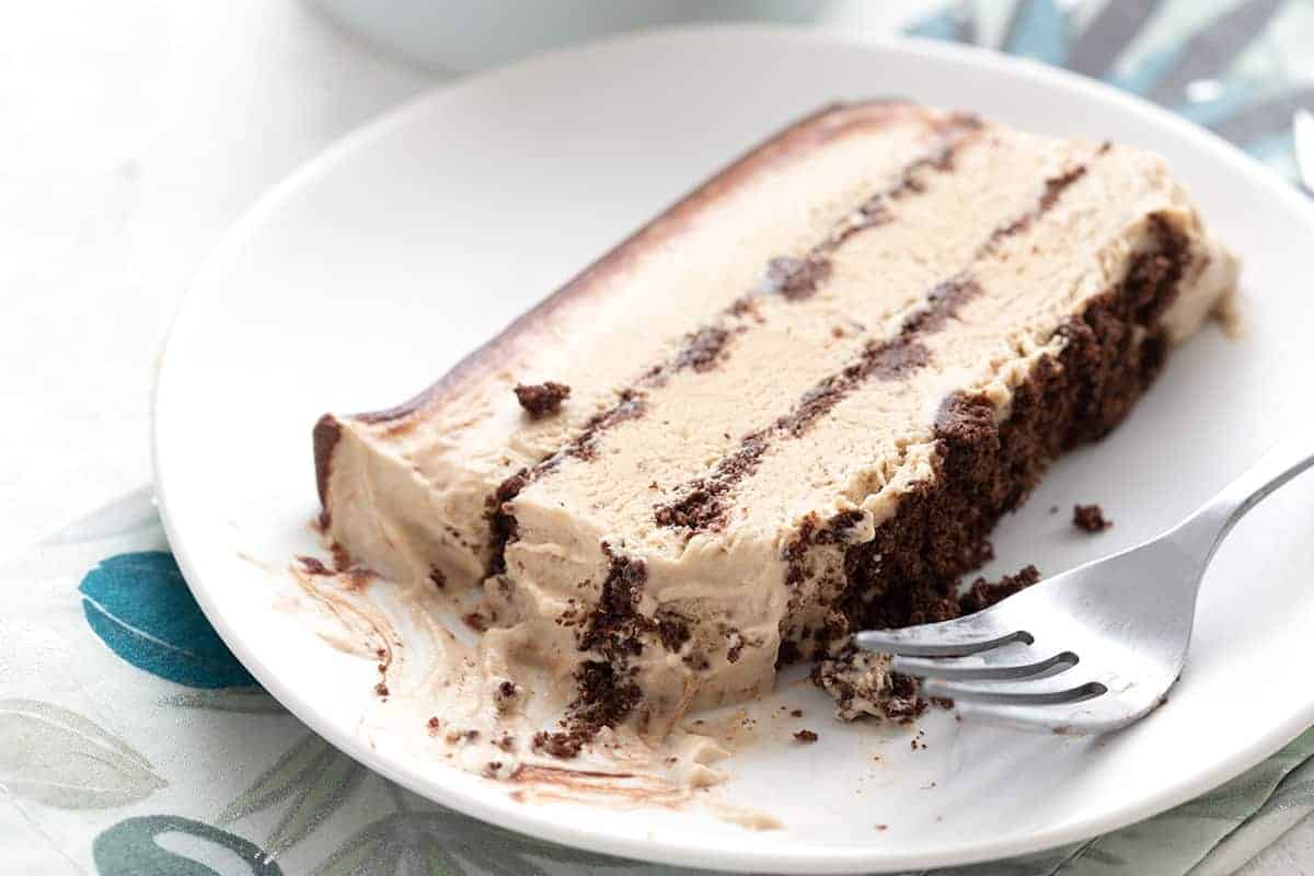 A slice of keto coffee ice cream cake on a white plate over a blue patterned napkin.