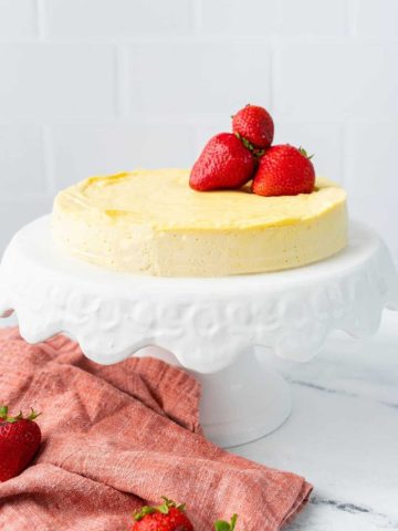 Crustless Keto Cheesecake on a white cake stand with strawberries on top.