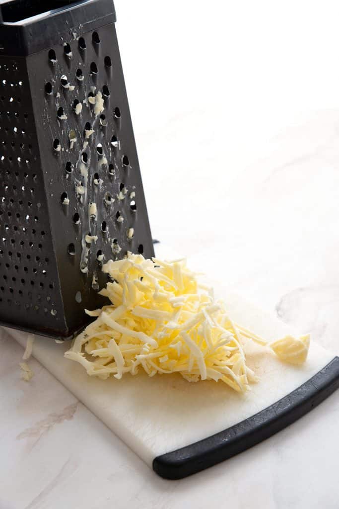 Frozen grated butter on a cutting board in front of a box grater.