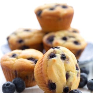 A stack of keto blueberry muffins on a white table with blueberries around it.
