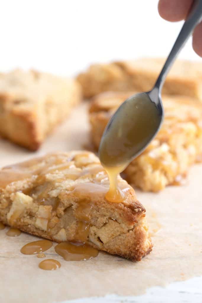 A spoon drizzling caramel sauce over a keto apple scone.