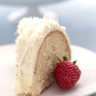 Titled image of a slice of keto coconut cake on a white plate with a strawberry.