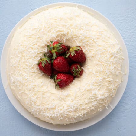 Top down image of a keto coconut bundt cake on a white plate with strawberries piled up in the center.