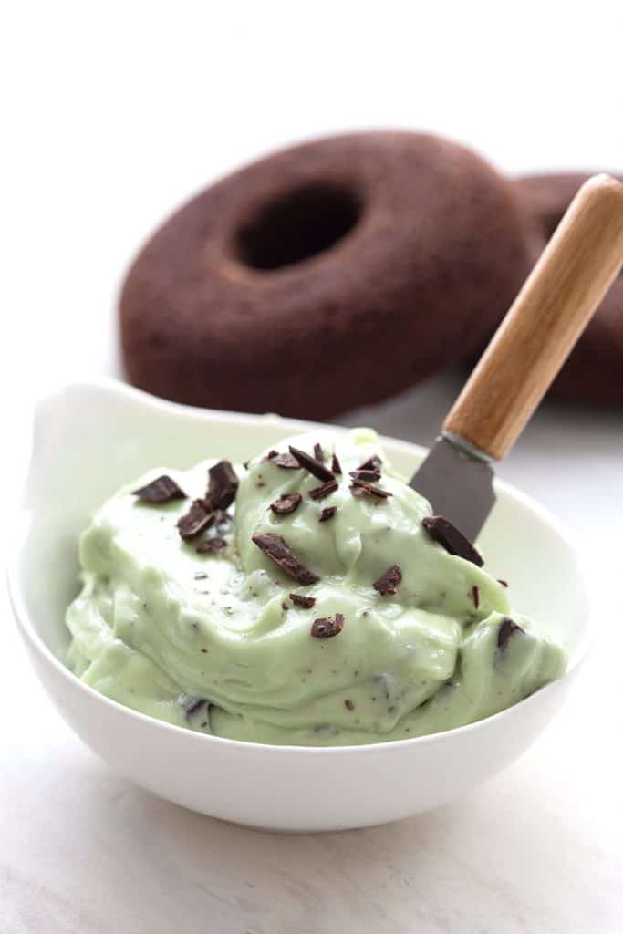 Close up shot of keto mint chip frosting with chocolate donuts in the background.