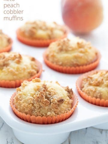 Titled image of keto peach muffins in a white ceramic muffin pan with a peach in the background.