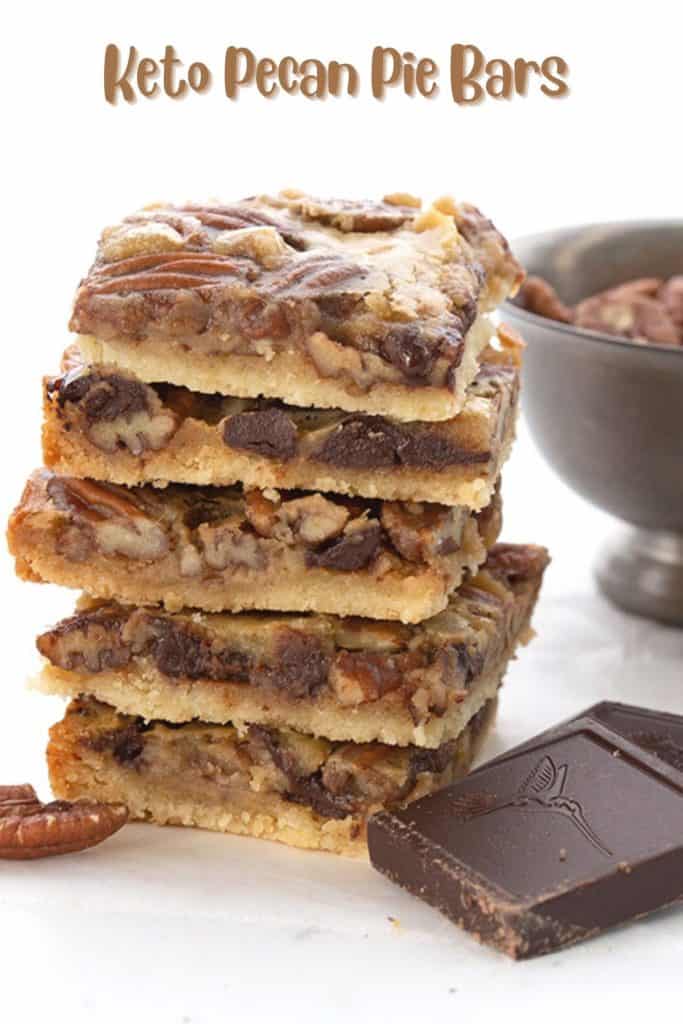 Titled image of a stack of keto pecan pie bars with a bowl of pecans and some chocolate.