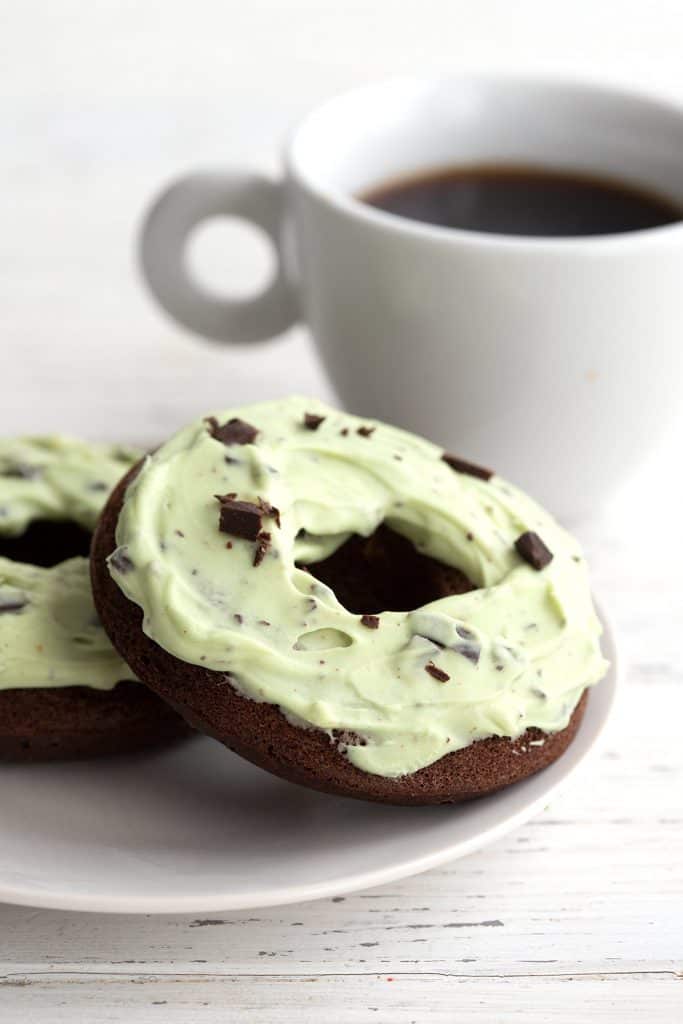 Two mint chip donuts sit on a white plate with a cup of coffee in the background.