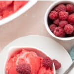 Top down image of sugar-free raspberry sorbet in a white bowl with a bowl of raspberries beside it.