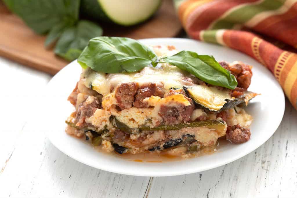 Close up shot of keto zucchini lasagna on a white plate with basil leaves on top.