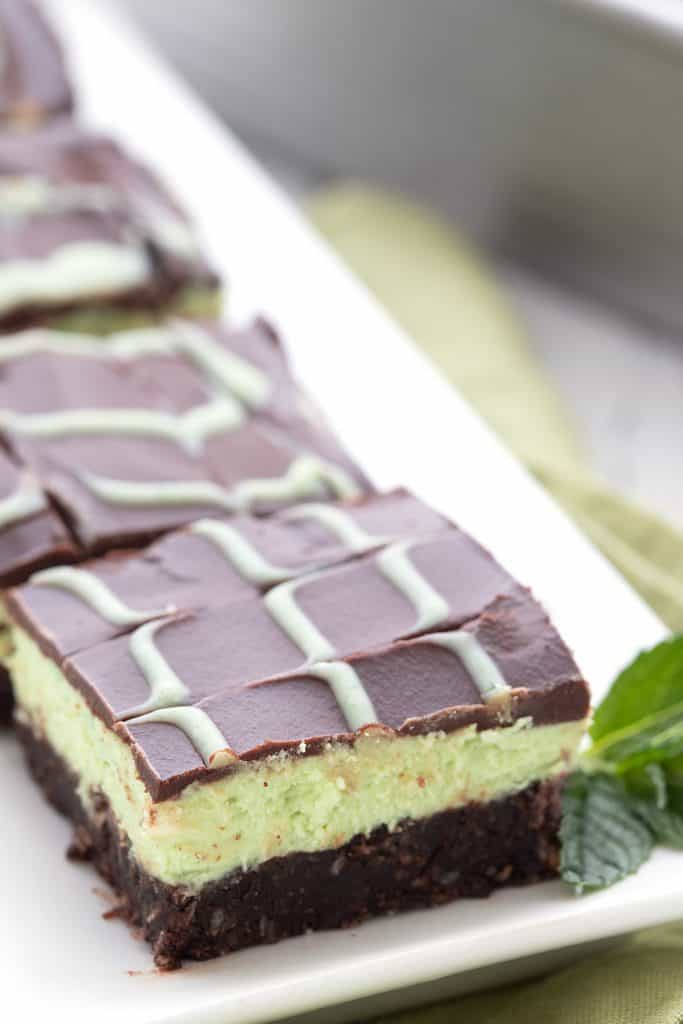 Keto no bake mint chocolate bars on a white platter with a sprig of mint.