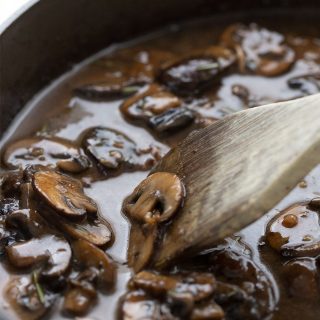 A pan full of keto mushroom gravy with a wooden spoon.