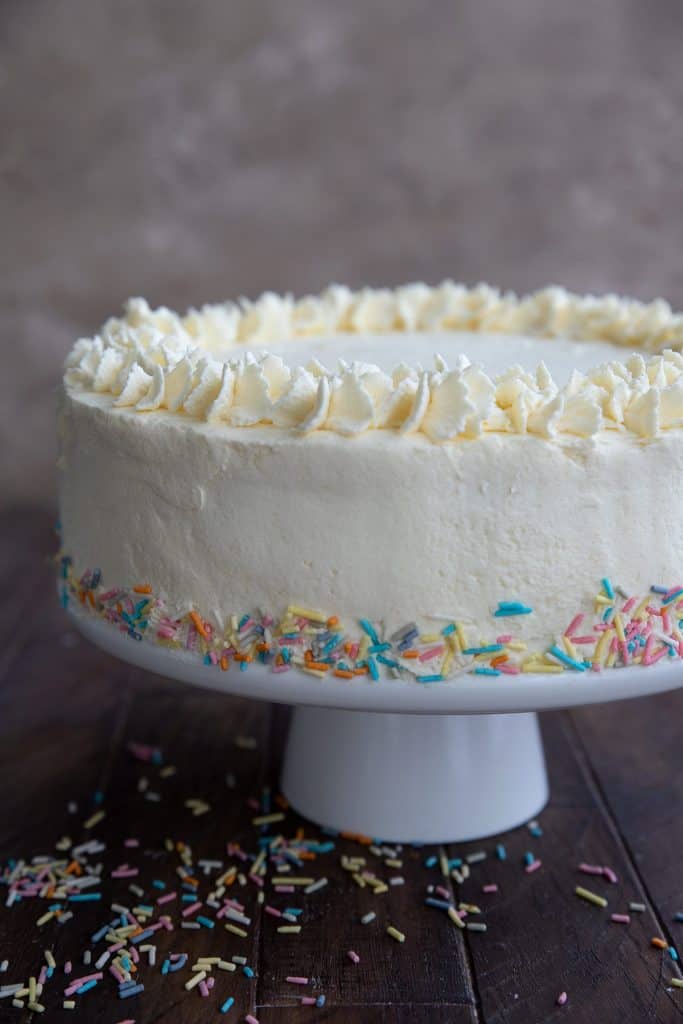 Keto Vanilla Cake on a cake stand with sprinkles all around.