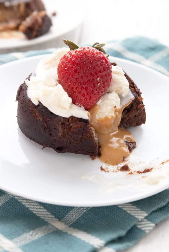 Keto chocolate peanut butter lava cake on a white plate with ice cream and a strawberry on top.