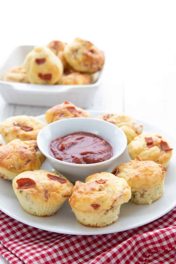 Mini keto pizza bites on a plate with a bowl of sugar free marinara sauce in the center.