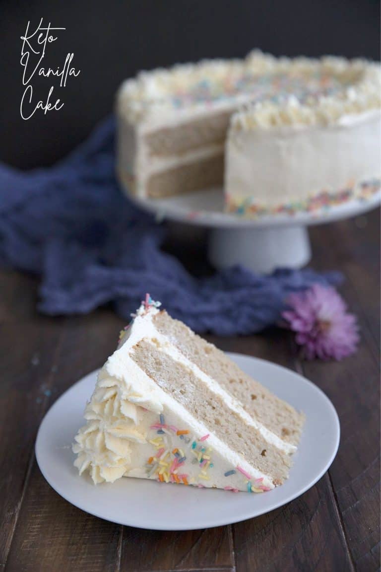 Titled image of a slice of keto vanilla cake on a white plate, in front of a cake plate with the rest of the cake.