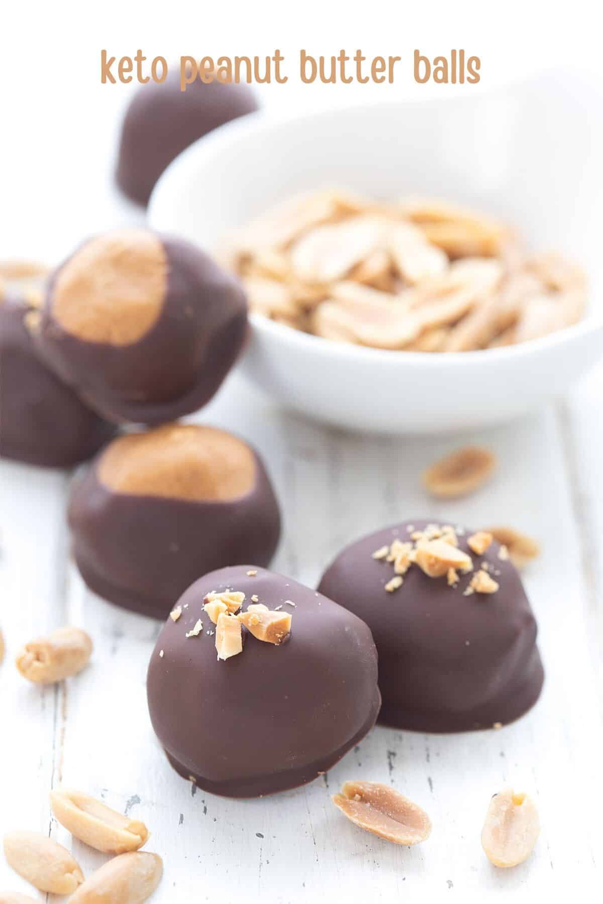 Titled image for keto peanut butter balls on a white wooden table with peanuts strewn around.