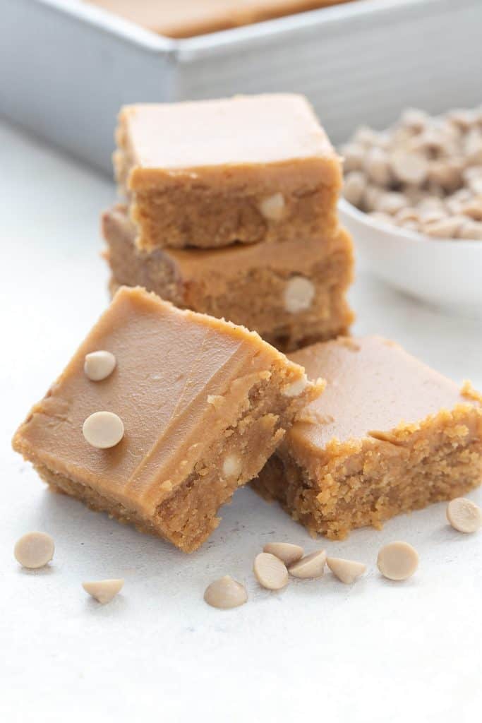 Keto peanut butter blondies in a pile in front of a bowl of sugar free peanut butter chips.