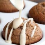 Titled image of a spoon drizzling glaze over a keto gingerbread muffin in a white muffin tin.