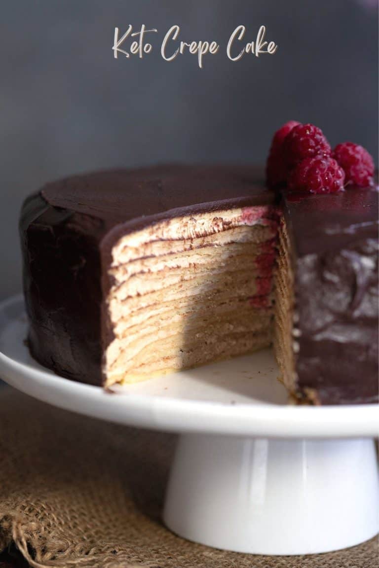 Keto crepe cake on a white cake plate with a slice cut out of it.