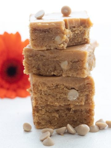 A stack of keto peanut butter blondies in front of an orange gerbera daisy.